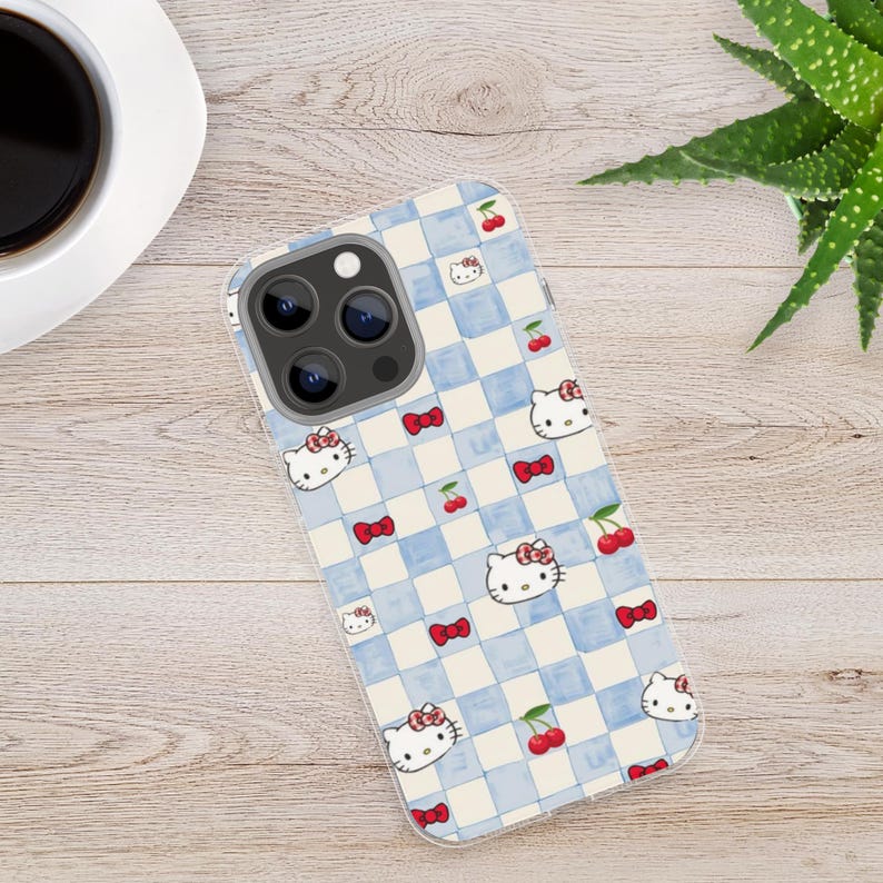 Puede incluir: Una funda transparente para tel&eacute;fono con un dise&ntilde;o de cuadros azules y blancos, decorada con Hello Kitty, lazos rojos y cerezas. La funda est&aacute; dise&ntilde;ada para un smartphone y tiene un recorte para la c&aacute;mara.