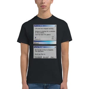 Op de afbeelding: Zwart T-shirt met een grappige computerfoutmelding. Het ontwerp bevat de tekst "Life.exe Error" en "Not Enough Coffee to Complete This Operation." Het shirt heeft een ronde hals en korte mouwen.