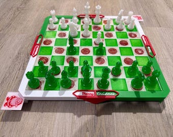 May include: A Christmas-themed chess set with green and white pieces on a green and white board. The board has red accents and the words "Merry Christmas" on the front. A small card with a red design is on the side.