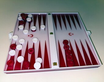 May include: A backgammon board with red and white playing pieces. The board is white with red triangular markings and a Turkish flag symbol. The game is open and ready to play.