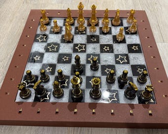 May include: A decorative chess set with a brown wooden frame. The chessboard features a black and white checkered pattern with star accents. The chess pieces are gold and black.