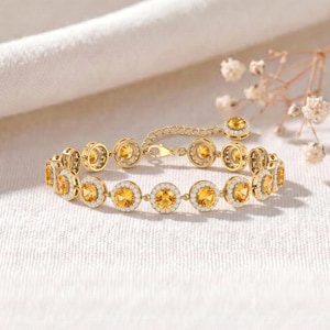 May include: A gold chain bracelet featuring a series of round, faceted yellow citrine gemstones, each encircled by a halo of small, clear white stones. The bracelet includes a delicate gold link chain and a secure clasp mechanism.