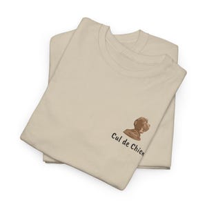 May include: Two beige t-shirts are neatly folded and stacked. The shirts feature a small brown dog graphic and the text "Cul de Chien" printed on the front. The shirts are made of a soft, comfortable material.