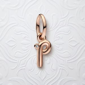 May include: Rose gold charm in the shape of the letter "P" with a small diamond accent. The charm has a polished finish and a loop for attaching to a bracelet or necklace. The charm is a pendant.