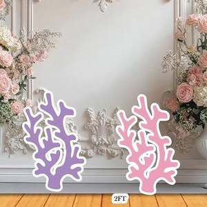 May include: Two coral-shaped decorations, one lavender and one pink, with white outlines, stand on a wooden surface. The background features a white wall with floral arrangements and decorative molding. The text "2FT" is visible.