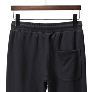 May include: Black sweatpants with a drawstring waistband and a single back pocket. The pants are hanging on a wooden hanger with a black metal hook. The fabric appears to be a soft, comfortable material.
