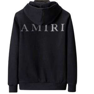 May include: Black hooded sweatshirt with the word "AMIRI" in silver lettering across the back. The sweatshirt has a drawstring hood and a kangaroo pocket. The fabric appears to be a soft material.