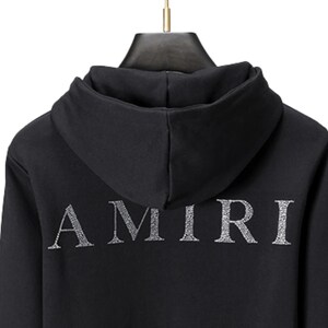 May include: Black hooded sweatshirt with the word "AMIRI" in silver, centered on the back. The hoodie has a drawstring and a hood. The fabric appears to be a soft material.