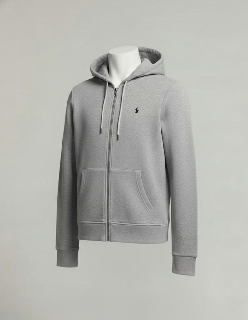 May include: A light gray zip-up hoodie with a drawstring hood and a kangaroo pocket. The hoodie features a small navy blue logo on the chest. The garment is displayed on a mannequin against a neutral background.