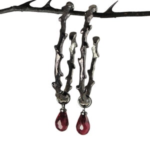 May include: A pair of silver hoop earrings shaped like thorny branches with dangling red gemstone drops.