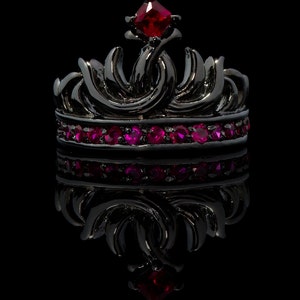 Peut inclure: Une couronne noire avec un bijou rouge sur le dessus et une rang&eacute;e de bijoux roses autour de la base.