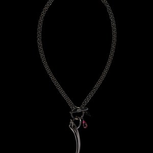 May include: A black chain necklace with a silver pendant featuring a long, curved tooth shape and a small red gemstone.