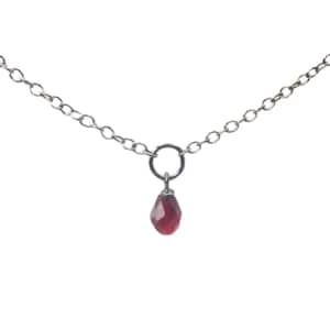 May include: A delicate silver chain necklace with a single, dangling, red gemstone pendant.