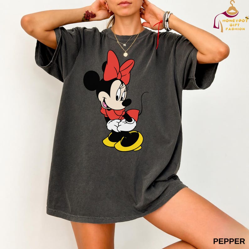 May include: A charcoal gray t-shirt featuring a Minnie Mouse graphic. Minnie is depicted in her classic outfit: a red bow, red dress, white gloves, and yellow shoes. The word "PEPPER" is printed in the bottom right corner.