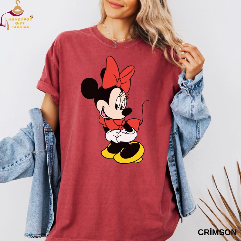 May include: Crimson-colored t-shirt featuring a graphic of Minnie Mouse in a red bow, dress, and shoes with yellow soles. The shirt has rolled-up sleeves and the word "CRIMSON" printed at the bottom right.