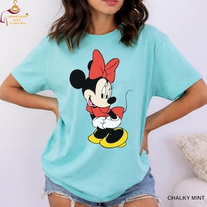 May include: A mint green t-shirt featuring a graphic of Minnie Mouse in a red bow, dress, and yellow shoes. The shirt has short sleeves and a relaxed fit. The text "CHALKY MINT" is printed at the bottom right.