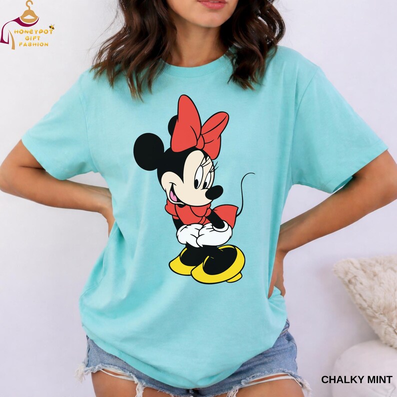 May include: A mint green t-shirt featuring a graphic of Minnie Mouse in a red bow, dress, and yellow shoes. The shirt has short sleeves and a relaxed fit. The text "CHALKY MINT" is printed at the bottom right.