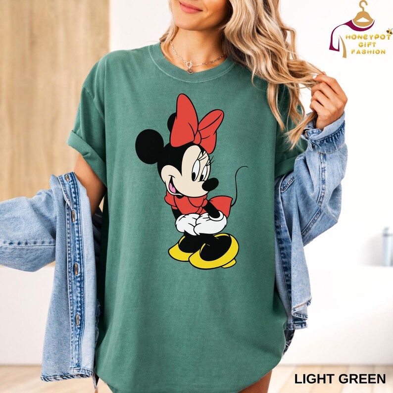 May include: Light green t-shirt featuring a Minnie Mouse graphic. The cartoon character is depicted in red, black, and yellow. The shirt has rolled-up sleeves and the text "LIGHT GREEN" is at the bottom.