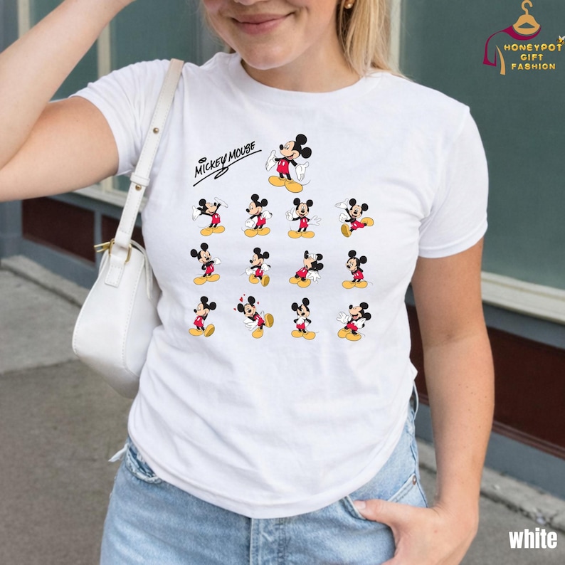 Może przedstawiać: Biała koszulka z grafiką Myszki Miki. Projekt zawiera wiele obraz&oacute;w Myszki Miki w r&oacute;żnych pozach, z napisem "Mickey Mouse" powyżej. Koszulka ma klasyczny okrągły dekolt.