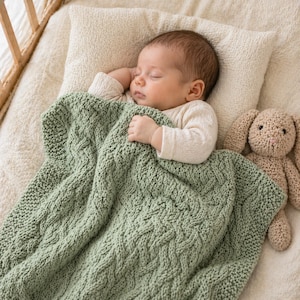Puede incluir: Un bebé dormido está acurrucado en una cuna, cubierto con una suave manta de punto verde salvia. Un juguete de conejo de punto beige descansa junto al bebé. El bebé lleva un body color crema y descansa sobre una almohada color crema.