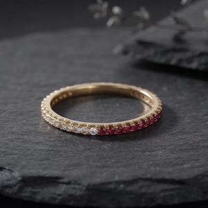 Könnte beinhalten: Ein dünner Goldring mit Pavé-Fassung, der auf einer Hälfte mit einer Reihe kleiner, klarer weißer Steine und auf der anderen Hälfte mit einer Reihe kleiner, leuchtend roter Steine besetzt ist. Der Ring hat eine polierte Metalloberfläche.