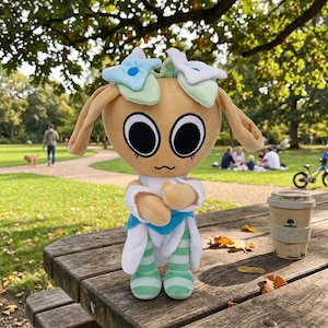 Pu&ograve; includere: Una bambola di peluche con la testa color beige, grandi occhi neri e lunghe orecchie flosce. Indossa un completo blu e bianco con gambe a righe verdi e bianche. La bambola &egrave; su un tavolo da picnic di legno in un parco.