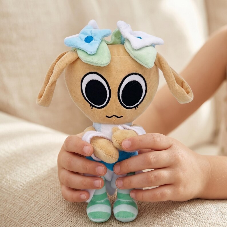 Pu&ograve; includere: Una bambola di peluche con una testa color beige, grandi occhi neri e una bocca piccola e curva. La bambola ha lunghe orecchie flosce ed &egrave; adornata da elementi a forma di fiore blu e bianco. Indossa un completo blu e bianco con piedi a righe verdi e bianche.