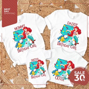The image is a collection of four white t-shirts featuring the character Ariel from the Disney movie "The Little Mermaid". The t-shirts are designed for different age groups, with the largest one for a 5-year-old and the smallest one for a younger child. The t-shirts are arranged on a bed of straw, creating a visually appealing display.
