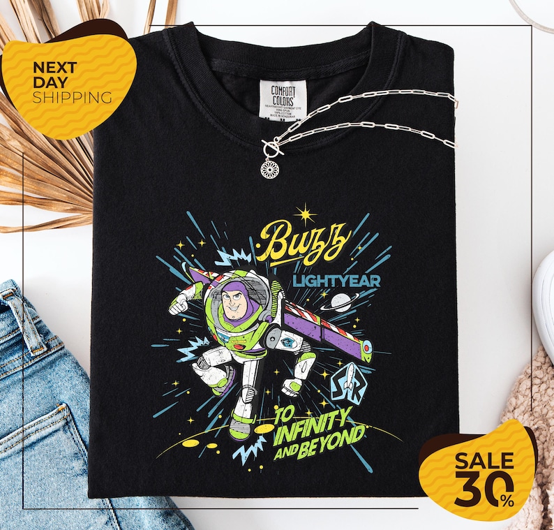 a black t-shirt with a colorful graphic of Buzz Lightyear from the Toy Story franchise, along with the text "Lightyear to Infinity and Beyond". The t-shirt is displayed on a white background, and there are yellow sale signs indicating a 30% discount.
