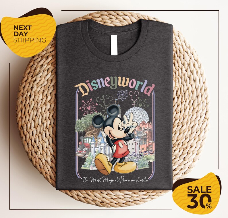 A t-shirt featuring a Mickey Mouse graphic with various Disney-themed elements, such as a castle, fireworks, and a sign that says "Disneyworld". The t-shirt is displayed on a woven placemat, and there are two yellow price tags in the image.