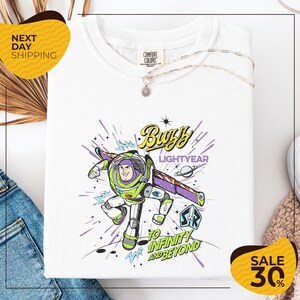 a white t-shirt with a colorful graphic design depicting Buzz Lightyear from the Toy Story franchise, along with the text "Lightyear to Infinity and Beyond". The t-shirt is displayed on a white background, and there are yellow and black sale signs indicating a 30% discount.