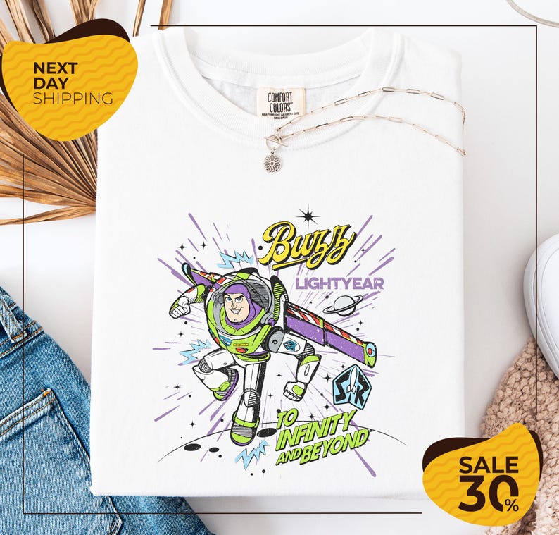 a white t-shirt with a colorful graphic design depicting Buzz Lightyear from the Toy Story franchise, along with the text "Lightyear to Infinity and Beyond". The t-shirt is displayed on a white background, and there are yellow and black sale signs indicating a 30% discount.