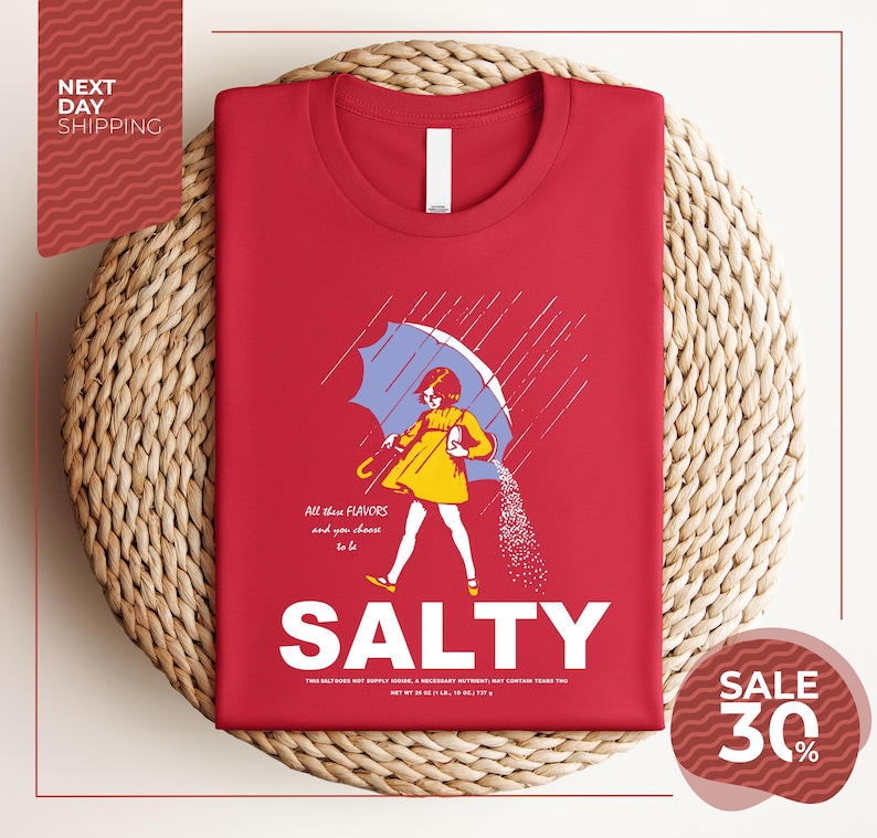 a red t-shirt with a graphic design depicting a woman holding a salt shaker and sprinkling salt on the ground, with the text "ALL these flavors and to be chosen" and "SALTY" below the image.