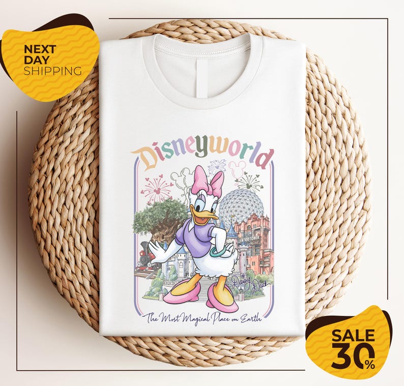 A white t-shirt with a Disney World-themed graphic design, featuring a cartoon image of a duck and various Disney landmarks.