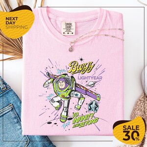 a pink t-shirt with a colorful graphic of Buzz Lightyear from the Toy Story franchise, along with the text "Lightyear to Infinity and Beyond". The t-shirt is displayed on a white background, and there are yellow and black sale signs indicating a 30% discount.