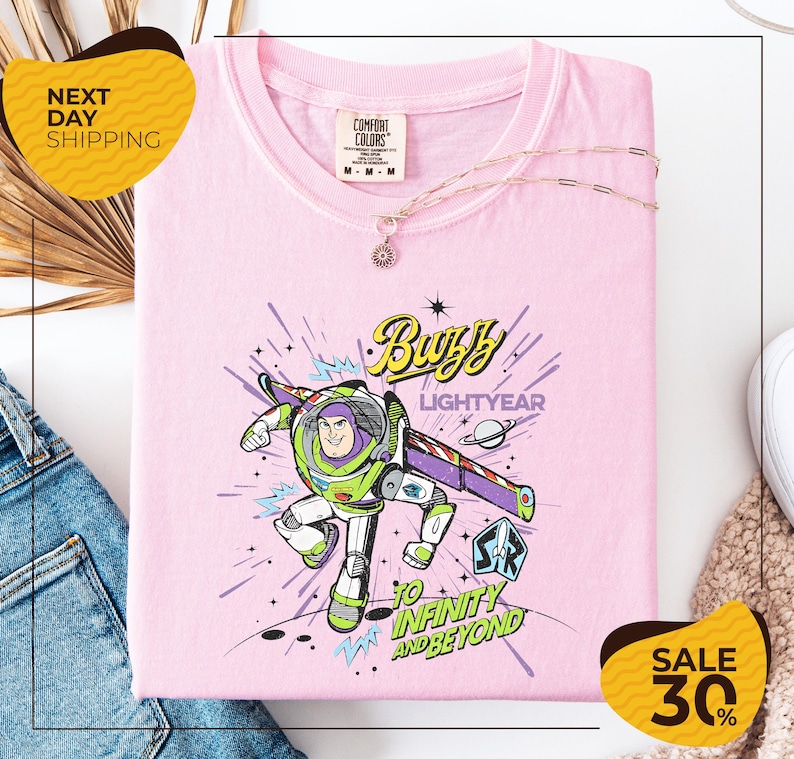 a pink t-shirt with a colorful graphic of Buzz Lightyear from the Toy Story franchise, along with the text "Lightyear to Infinity and Beyond". The t-shirt is displayed on a white background, and there are yellow and black sale signs indicating a 30% discount.