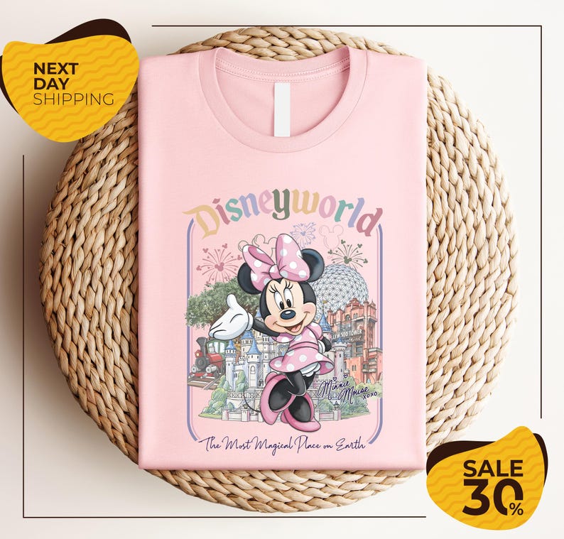 A pink t-shirt with a Minnie Mouse graphic and the text "Disneyworld" printed on it, placed on a woven basket.