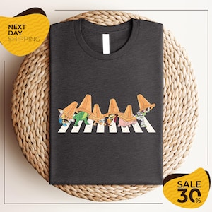 a gray t-shirt with a graphic design of cartoon characters crossing a crosswalk.
