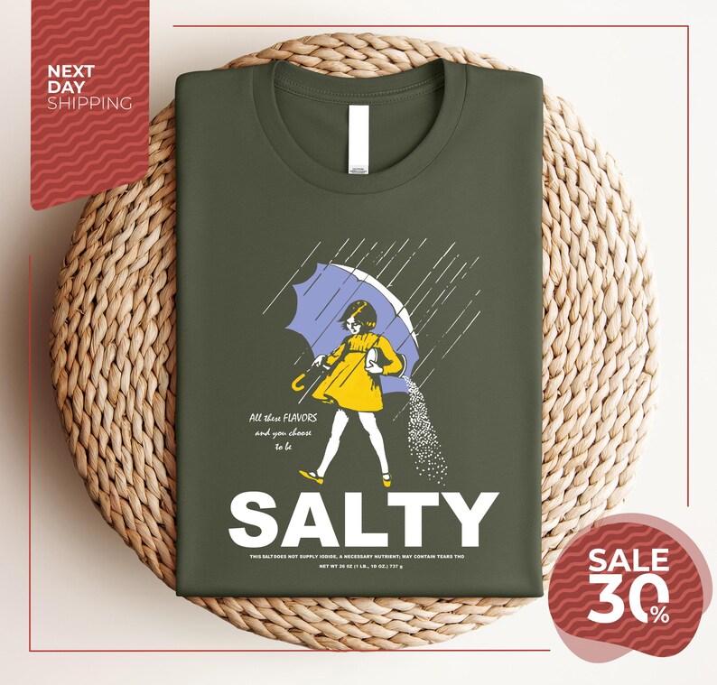 a green t-shirt with a graphic design depicting a person holding an umbrella and sprinkling salt on the ground. The text on the t-shirt reads "All these flavors and to be chosen are Salty", and there is a sale offer of "SALE 30%".