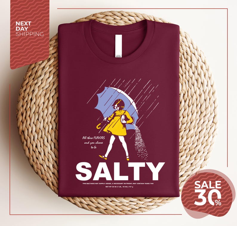 a maroon t-shirt with a graphic design depicting a woman holding an umbrella and sprinkling salt on the ground. The text on the t-shirt reads "ALL these flavors and to be chosen, SALTY" and "SALE 30%".