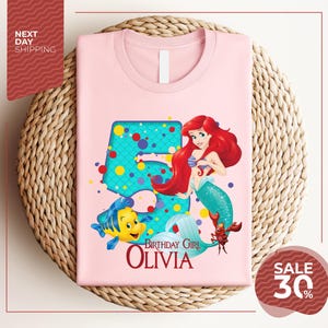 A pink t-shirt featuring a character from the Disney movie "The Little Mermaid" and the text "Birthday Girl Olivia" printed on it.