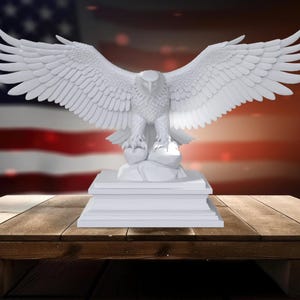 K&ouml;nnte beinhalten: Eine wei&szlig;e Adler-Skulptur mit ausgebreiteten Fl&uuml;geln, die auf einem rechteckigen Sockel steht. Der Adler ist detailliert mit strukturierten Federn. Im Hintergrund eine amerikanische Flagge und ein Holztisch.
