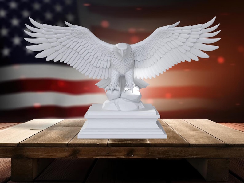 K&ouml;nnte beinhalten: Eine wei&szlig;e Adler-Skulptur mit ausgebreiteten Fl&uuml;geln, die auf einem rechteckigen Sockel steht. Der Adler ist detailliert mit strukturierten Federn. Im Hintergrund eine amerikanische Flagge und ein Holztisch.