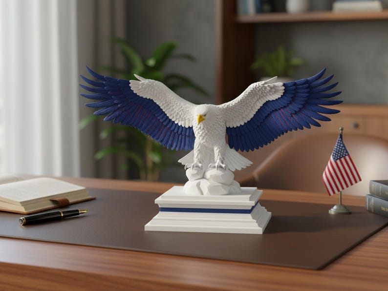 K&ouml;nnte beinhalten: Eine wei&szlig;e und blaue Adlerstatue mit ausgebreiteten Fl&uuml;geln, die auf einem wei&szlig;en Sockel mit blauen Akzenten sitzt. Der Adler hat einen gelben Schnabel und wird auf einem Schreibtisch mit einer kleinen amerikanischen Flagge ausgestellt.