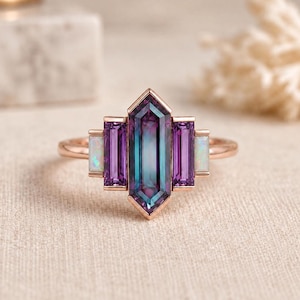 Peut inclure: Une bague en or rose ornée d'une pierre d'alexandrite hexagonale allongée au centre, flanquée de deux pierres d'améthyste violettes rectangulaires et de deux opales blanches plus petites, disposées géométriquement sur un anneau fin en or rose.