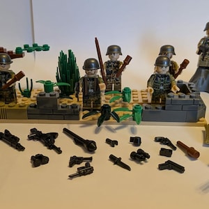 May include: A collection of toy soldiers and military accessories, including rifles, machine guns, and pistols. The set features miniature figures in military uniforms, along with a diorama of a battlefield setting. The color palette includes greens, browns, and greys.