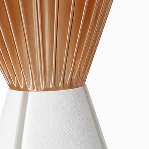 Pode incluir: Close-up de uma l&acirc;mpada moderna. A parte superior &eacute; dourada met&aacute;lica quente com ranhuras verticais. A base &eacute; branca texturizada, com formato geom&eacute;trico. A l&acirc;mpada est&aacute; em um fundo branco.