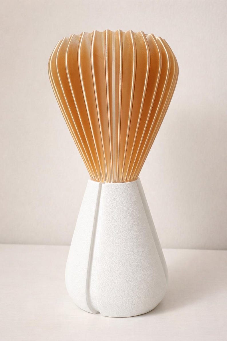 Pode incluir: Um vaso decorativo moderno com uma base geom&eacute;trica branca e um topo em forma de leque feito de ripas de madeira verticais castanho-claro. O vaso tem um design &uacute;nico e contempor&acirc;neo.