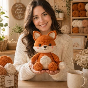 May include: A handcrafted crochet fox plush toy featuring vibrant orange and cream yarn, pointed ears, black safety eyes, a small embroidered nose, and a round belly. The stuffed animal is designed with a seated posture and a bushy tail.