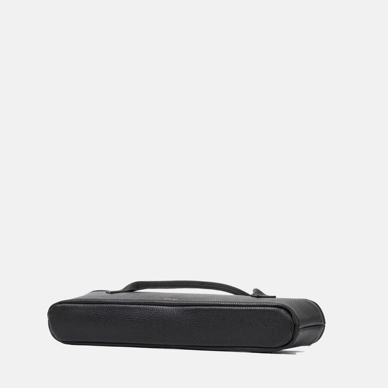 May include: A black, rectangular, pebbled-texture case with rounded corners and a slim profile. The case features a top-mounted handle and a zipper closure that runs along the perimeter, providing a secure and compact storage solution for small items.
